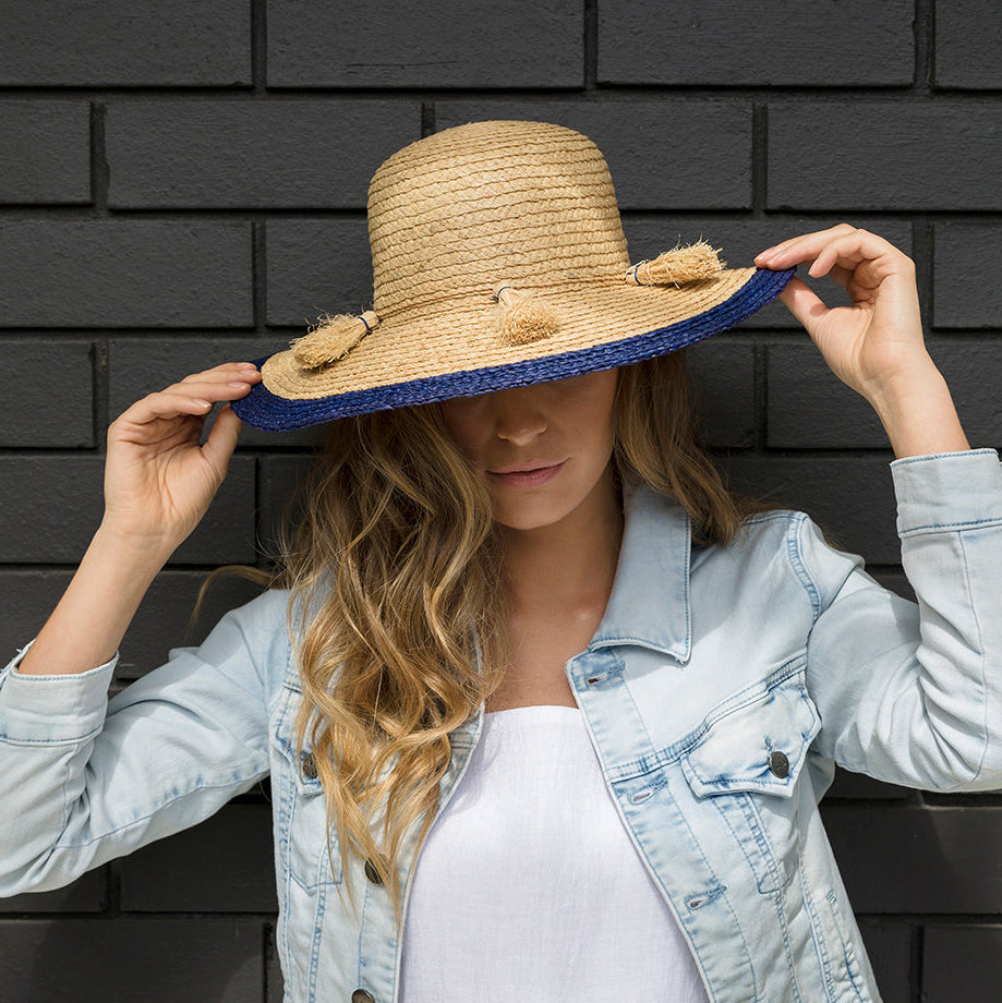 Woman wearing Mexicoma natural raffia wide-brim hat with deep sea blue edge band
