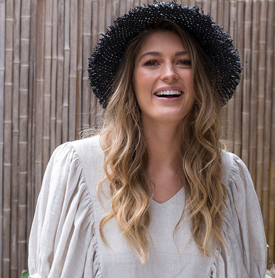 If It Glitters paper hat with black grosgrain band and hand-cut fringe on woman looking ahead smiling