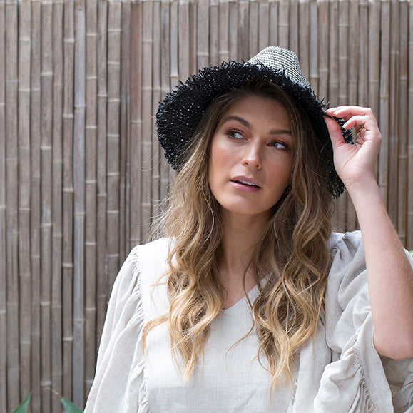 If It Glitters paper hat with black grosgrain band and hand-cut fringe on woman looking side on