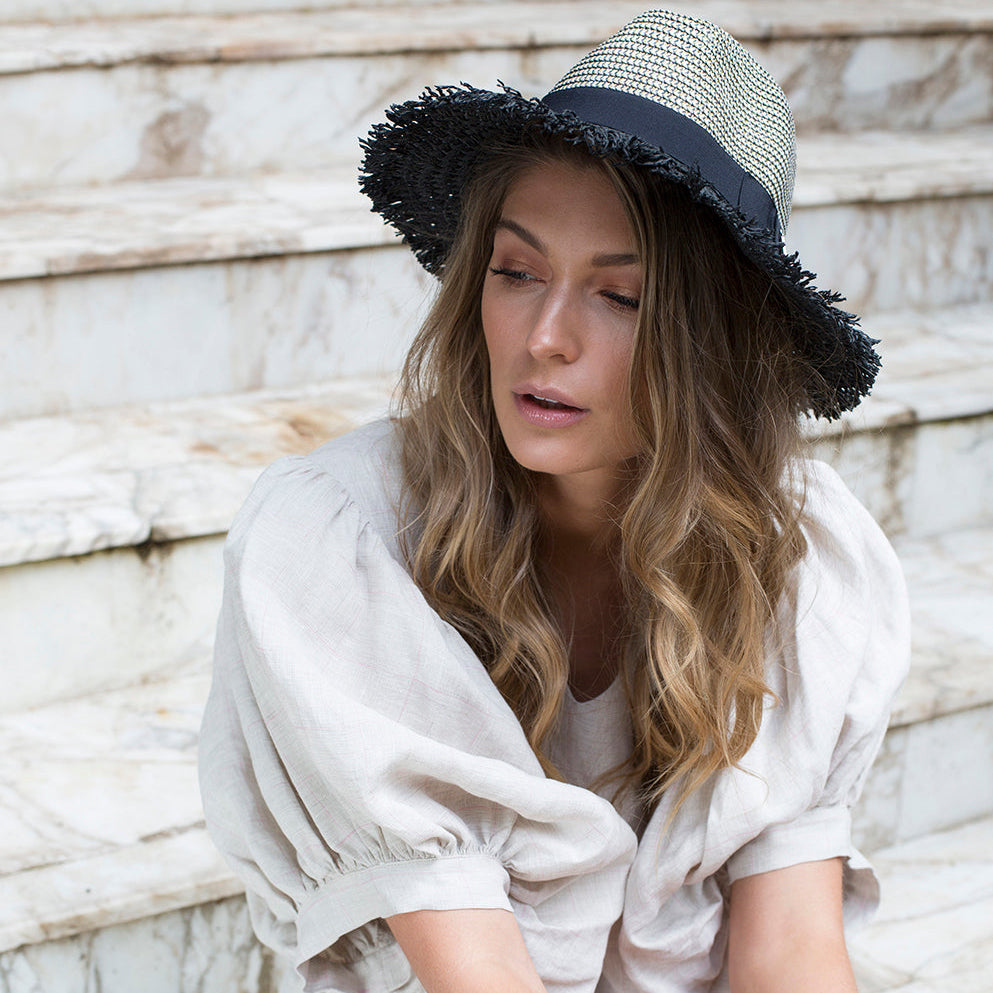 If It Glitters paper hat with black grosgrain band and hand-cut fringe on woman looking down
